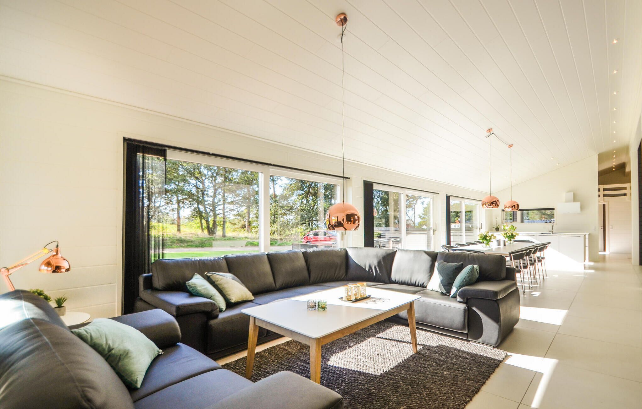 Uma sala de estar moderna com um sofá seccional, uma mesa de centro e grandes janelas com vista para o exterior.