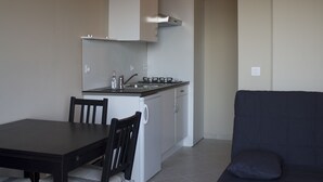A compact kitchen with a dining table and chairs, a sofa, and a built-in oven. - Villas Lidia - Fengari (Livadi)