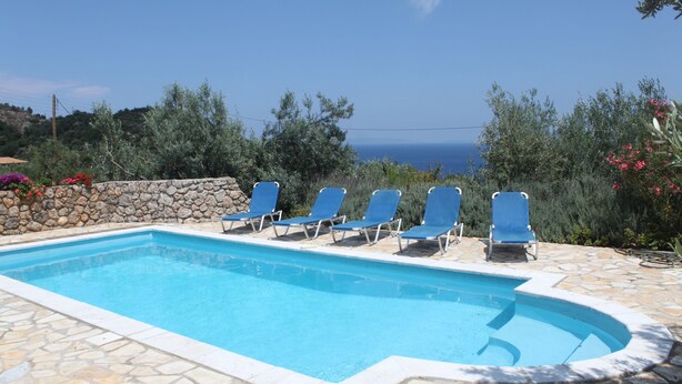 A swimming pool with blue chairs and a stone wall. - Villas Lidia - Fengari (Livadi)