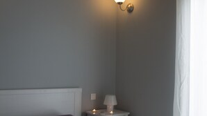 A bedroom with a bed, bedside table, lamp, and wall-mounted light fixture. - Villas Lidia - Fengari (Livadi)