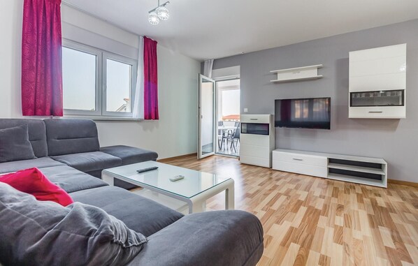 Una sala moderna con un sofá gris, una mesa de centro de vidrio y un televisor de pantalla plana montado en la pared.