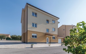 Un edificio residencial de varios pisos con techo plano, entrada central y un pequeño jardín delantero.