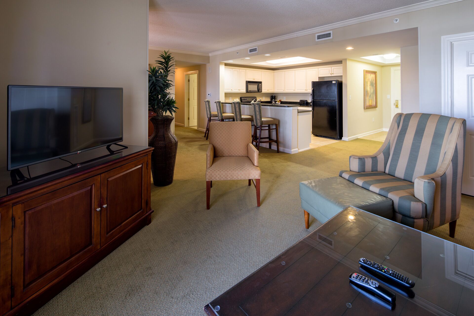 A living room with a flat-screen TV, a wooden cabinet, a beige armchair, a striped sofa, and a glass coffee table.