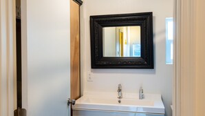A bathroom with a white sink, a black-framed mirror, and a door with a wooden panel. - Downtown Cozy Condo- Walk to Best Diners, Breweries, NAU, Historic Flagstaff! (Flagstaff)