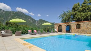 Area piscina con lettini e ombrelloni, un edificio in pietra con finestre ad arco e montagne sullo sfondo.