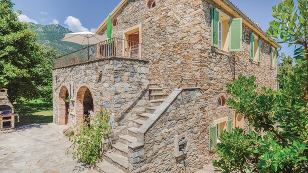 Un edificio in pietra con un balcone, una scala e un piccolo giardino.