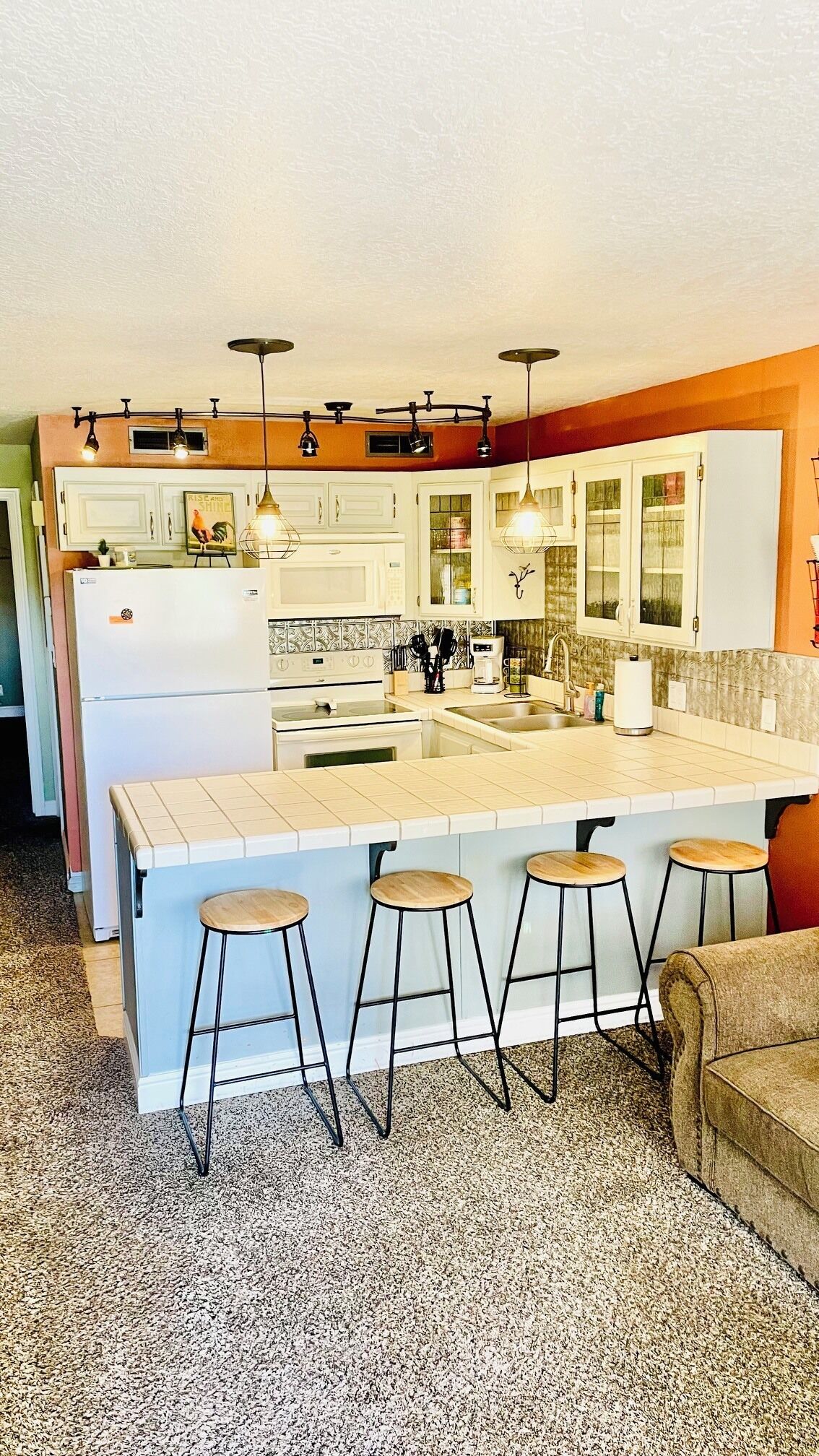 A kitchen with a central island, bar stools, pendant lights, and a refrigerator.