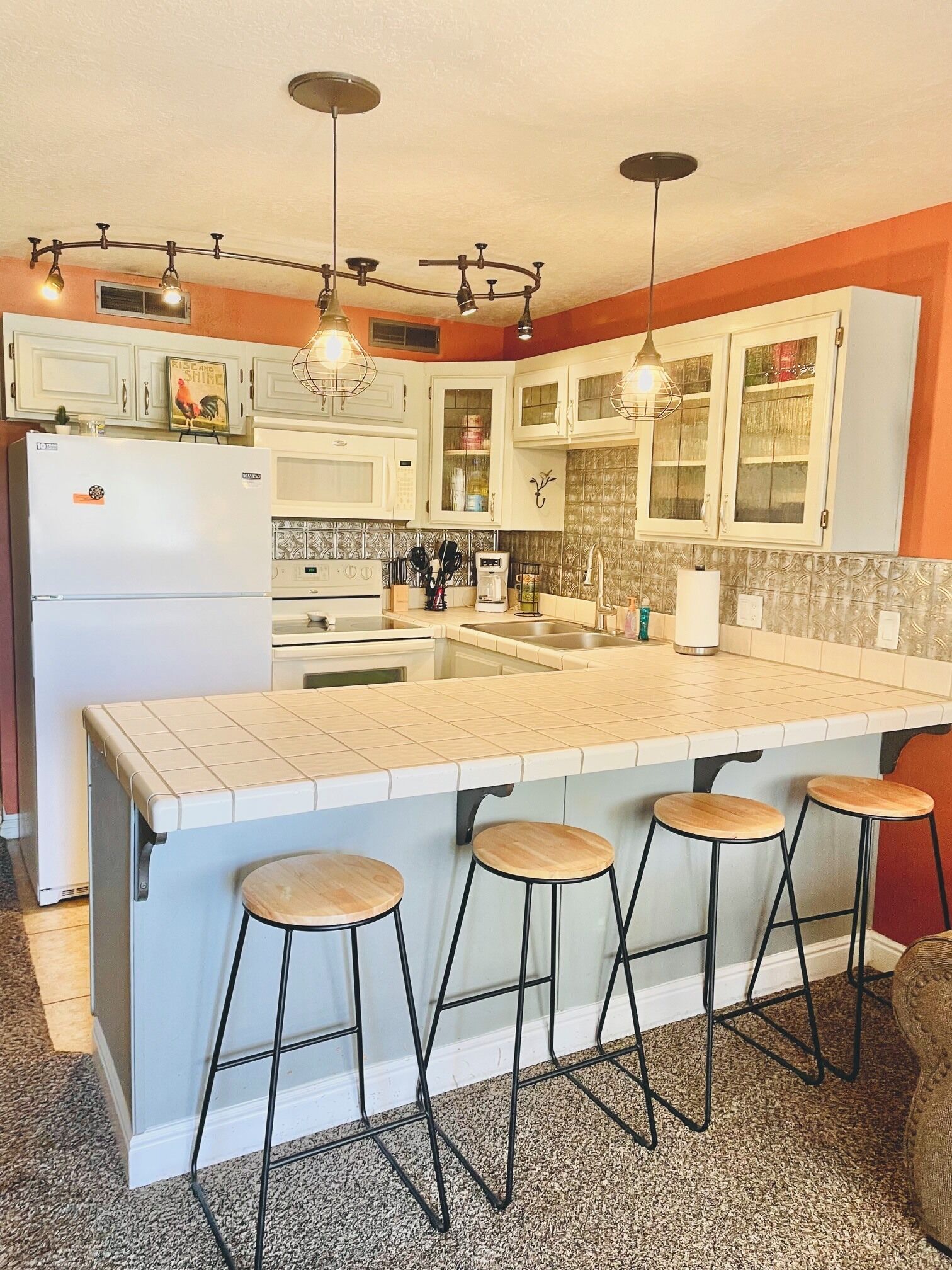 A kitchen with a central island, bar stools, white cabinets, a refrigerator, and pendant lighting.