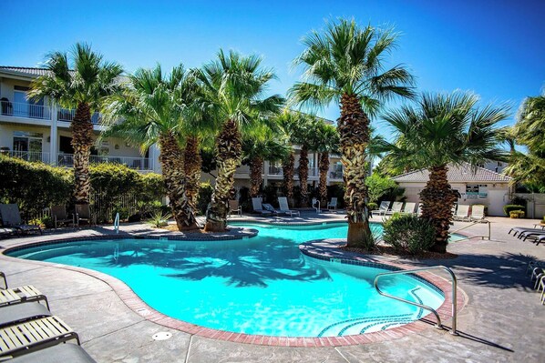 Una piscina rodeada de palmeras, sillas de descanso y un edificio con balcones.