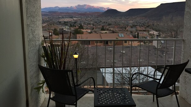 Ein Balkon mit zwei Stühlen und einem Tisch, der auf eine Stadt mit Bergen im Hintergrund blickt.