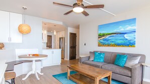 Een moderne woonkamer met een houten salontafel, een grijze bank met blauwe kussens, een schilderij van een landschap en een plafondventilator.
