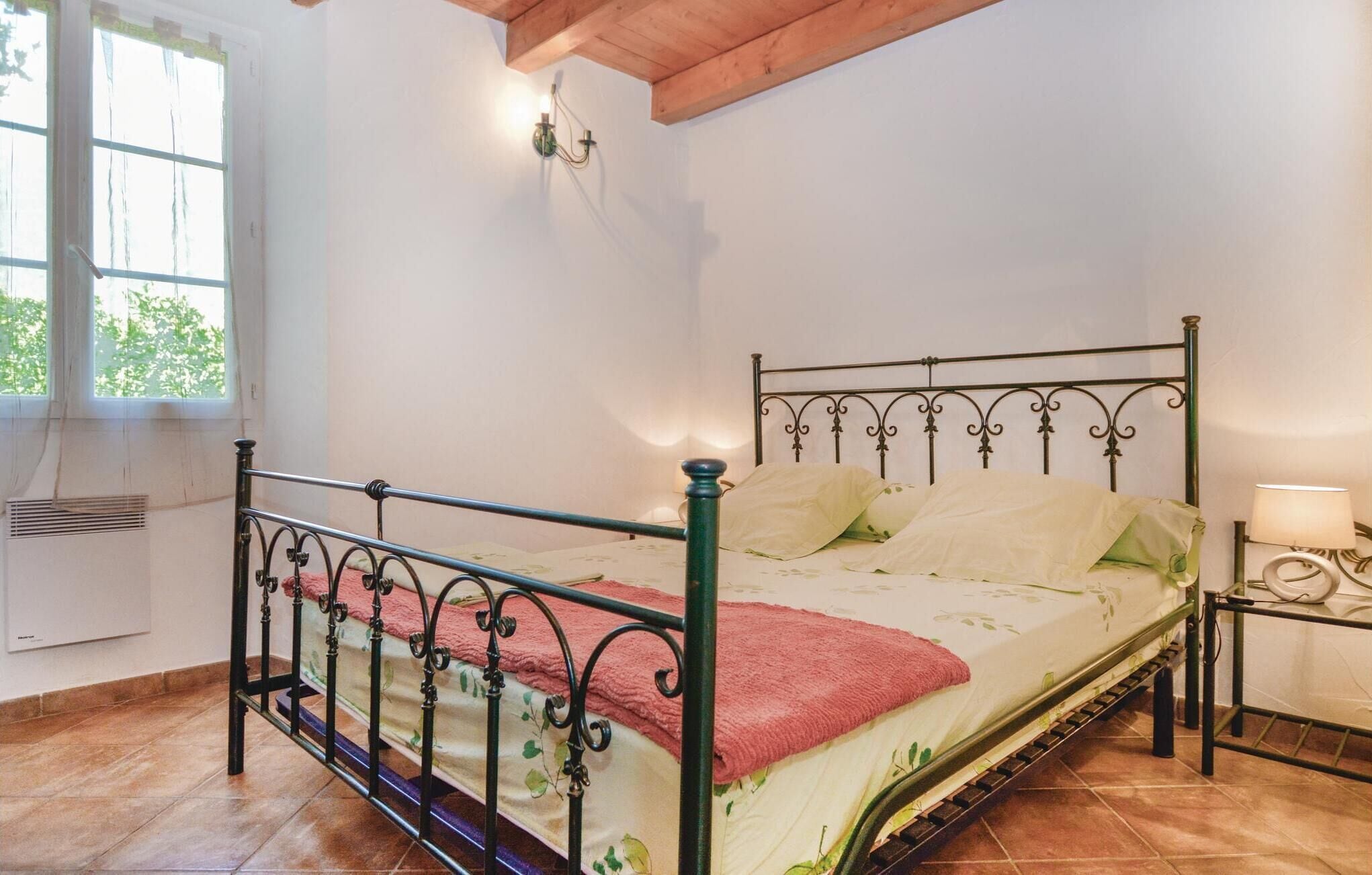 Een enkel bed met een metalen frame, een nachtkastje met een lamp en een raam met gordijnen.