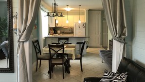 A living room with a dining area, a kitchen in the background, and a sofa with a zebra-patterned pillow.