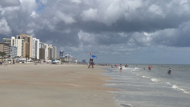 A beach with a cityscape in the background, including tall buildings and a lifeguard tower.