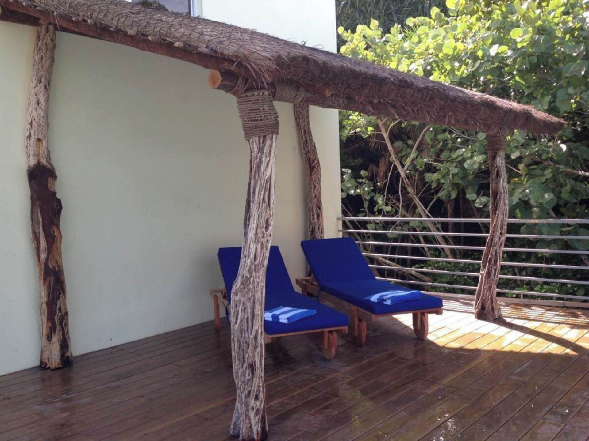 Une terrasse en bois avec deux chaises longues bleues et une structure de toit en chaume.