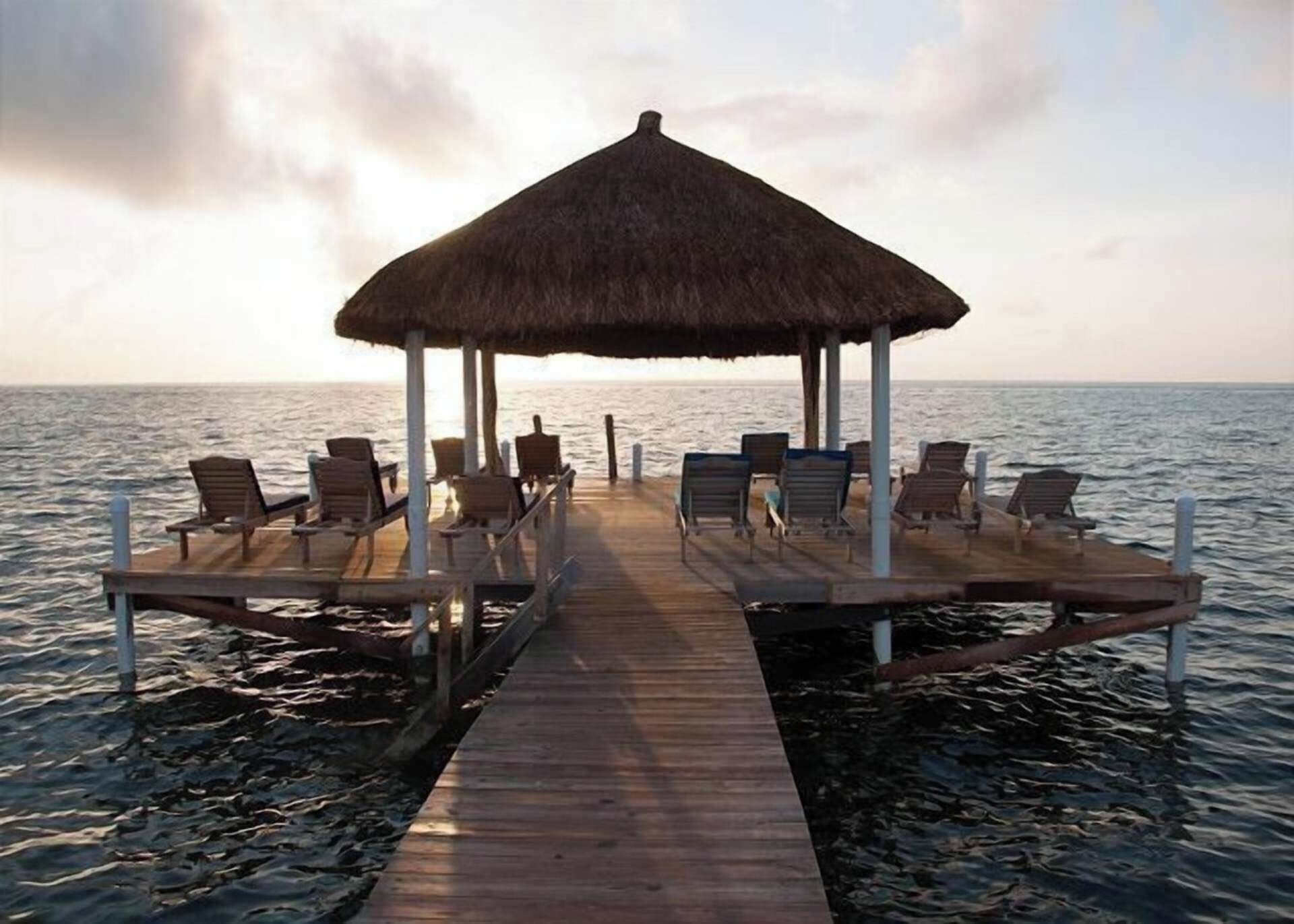 A wooden pier leading to a thatched-roof structure with several lounge chairs.