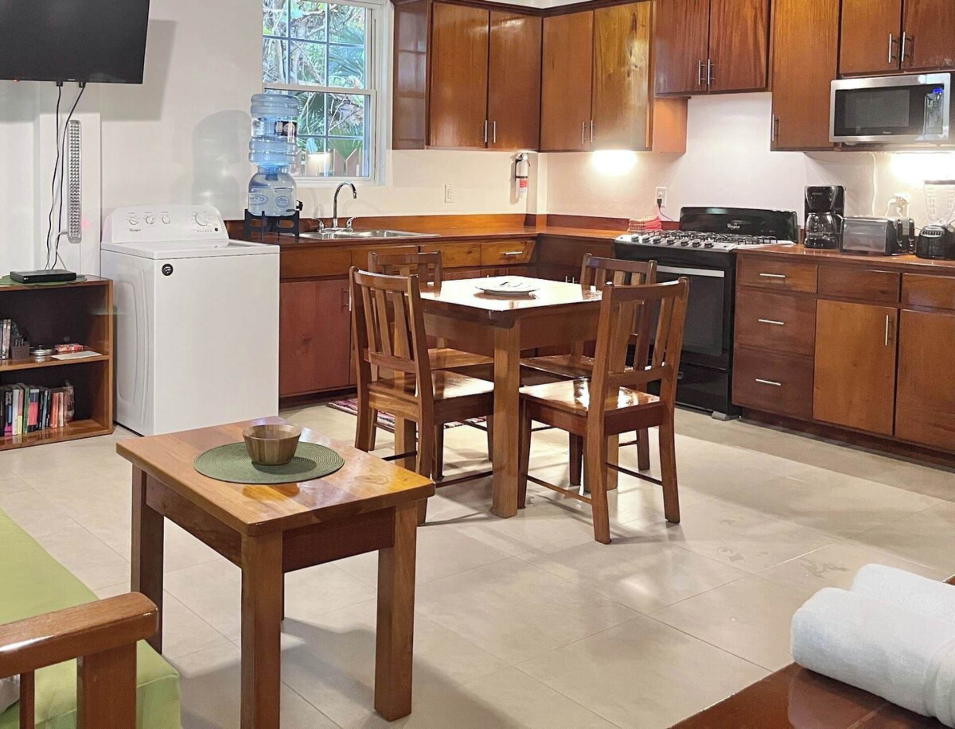 A compact kitchen with wooden cabinets, a dining table with chairs, a built-in oven, and a microwave.