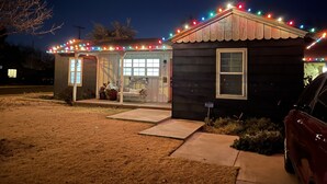 Ein kleines Haus mit Veranda, einem 'Frohe Weihnachten'-Schild und bunten Lichtern.