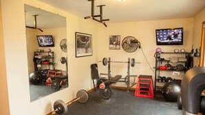 Een sportschool met spiegels, gewichthefapparatuur, een televisie en een ventilator.