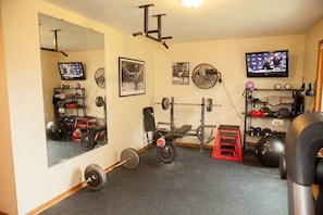 Ein Fitnessstudio mit Spiegel, Gewichten, einem Fernseher und einem Ventilator.