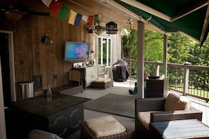 Un espacio de estar al aire libre con techo, mobiliario de mimbre, televisor y una parrilla.
