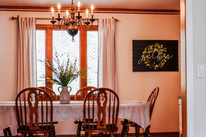 A dining area with a table set for four, wooden chairs, a chandelier, and a window with curtains.