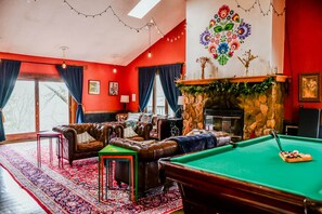 A room with a pool table, leather sofas, a fireplace, and a red wall with a floral mural.