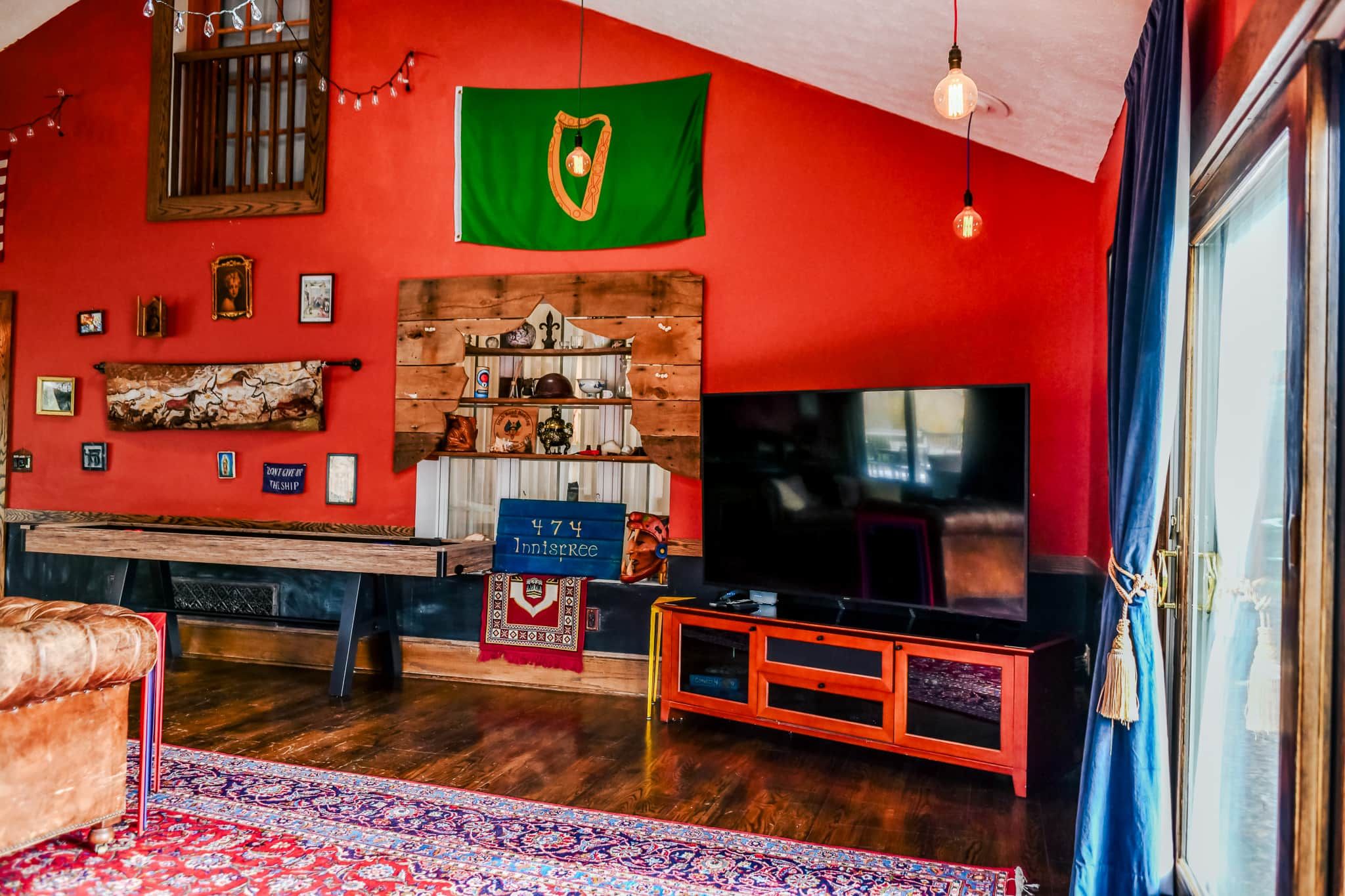 A living room with a red wall, a wooden entertainment unit, a television, and a flag.