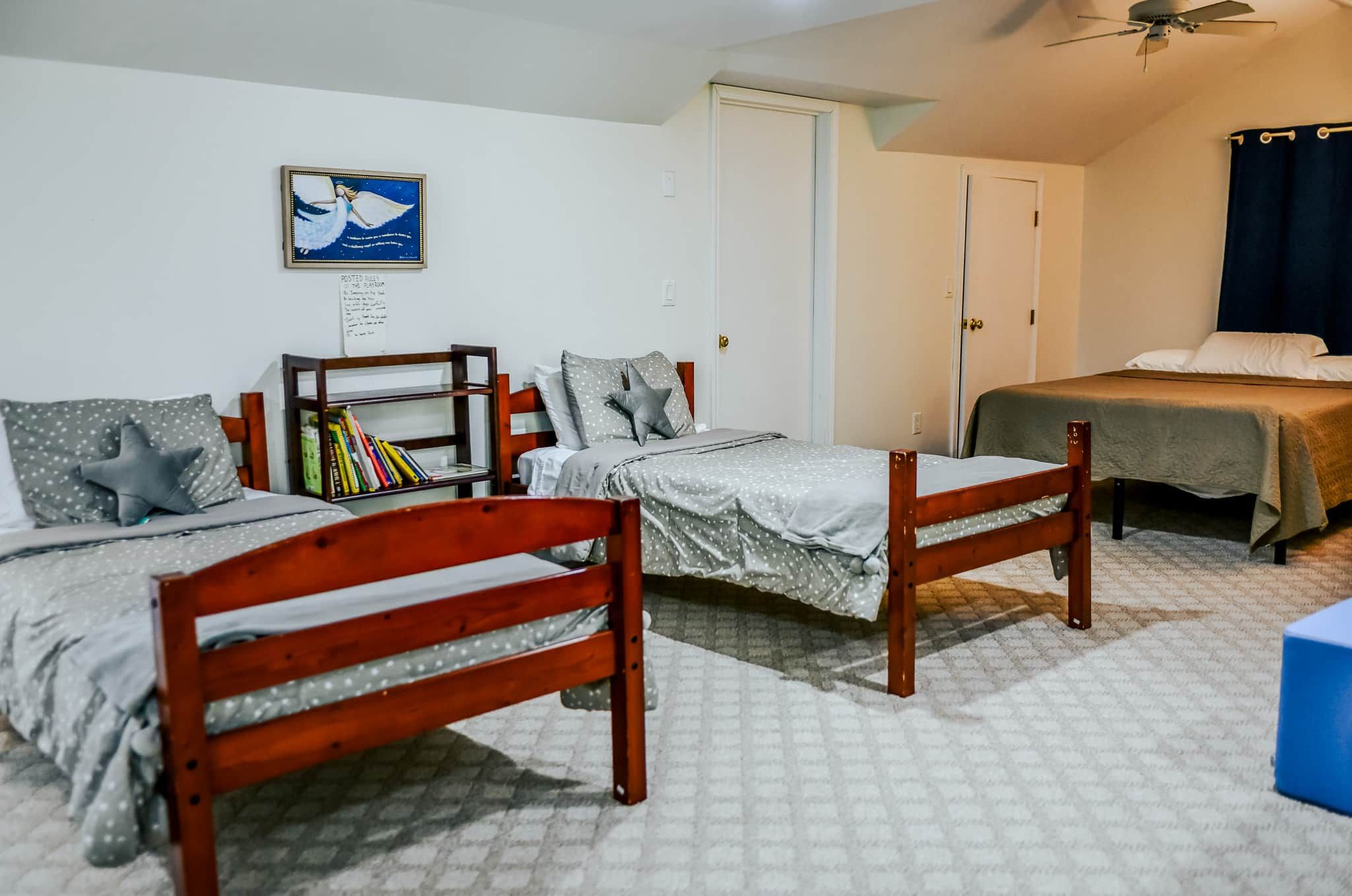A dormitory room with two wooden beds, a bookshelf, and a ceiling fan.