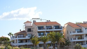 Un immeuble d’appartements à plusieurs étages, doté de balcons et entouré de palmiers et d’arbustes.