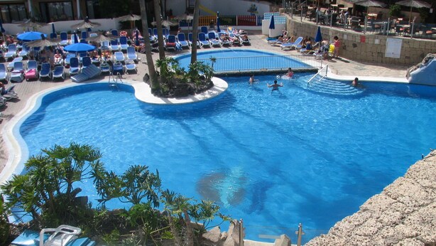 Une grande piscine dotée de plusieurs couloirs, entourée de chaises longues et de parasols.