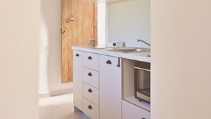A modern kitchen with white cabinets, a wooden door, and a stainless steel sink. - The Papas House on the Hill (Kamilari)