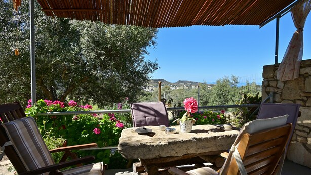 An outdoor seating area with stone tables and chairs, surrounded by lush greenery and flowers. - The Papas House on the Hill (Kamilari)