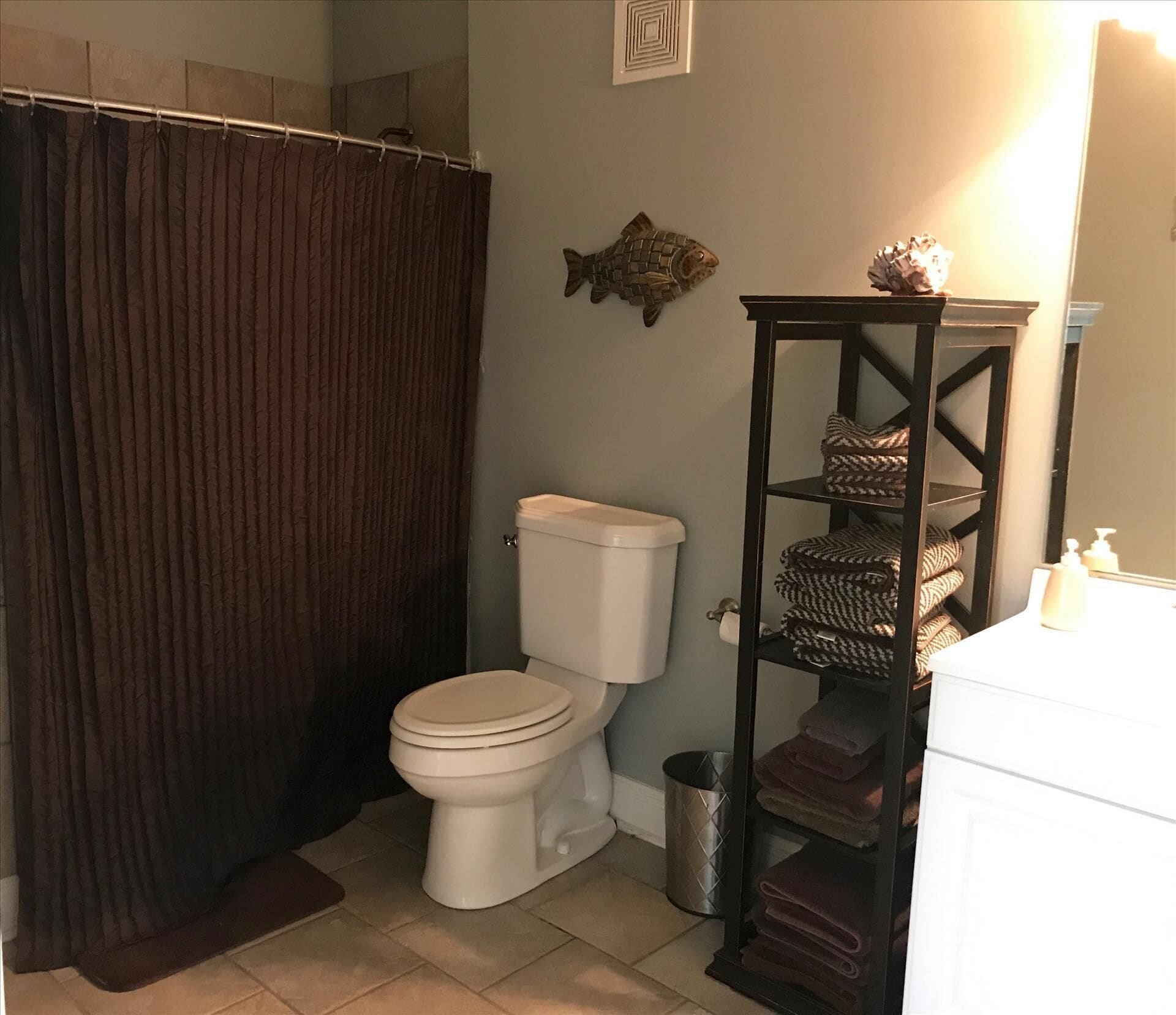 Un bagno con il water, una tenda della doccia, uno scaffale con asciugamani e un pesce decorativo al muro.