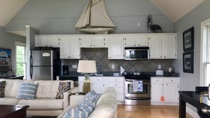 A modern kitchen with white cabinets, a stainless steel refrigerator, and a microwave. There is a dining area with a black table and chairs. - Peaceful Gulf Getaway - Close to Old Town Bay St Louis (Bay St Louis)