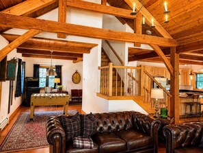 A spacious loft-style room with exposed wooden beams, a leather sofa, a foosball table, and a staircase leading to another level.