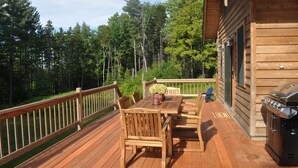 A wooden deck with a table and chairs, a barbecue grill, and a cabin in the background. - Luxurious Mountain Cabin near Okemo with High-End Modern Amenities for up to 12 (Ludlow)