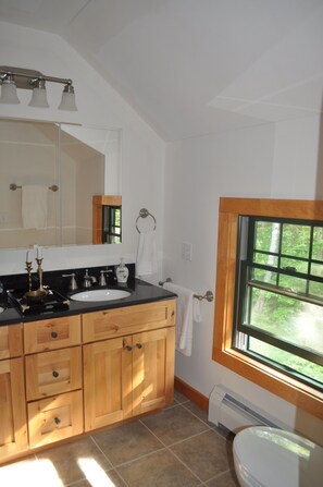 Un baño con tocador de madera, un espejo grande, una ventana con vistas y un inodoro blanco.