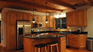 A kitchen with wooden cabinets, stainless steel appliances, a large island with stools, and pendant lighting. - Luxurious Mountain Cabin near Okemo with High-End Modern Amenities for up to 12 (Ludlow)