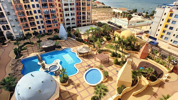Een resort met diverse zwembaden, palmbomen en uitzicht op de zee.