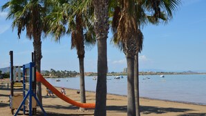 Een strand met palmbomen, een speeltuin en boten in het water.