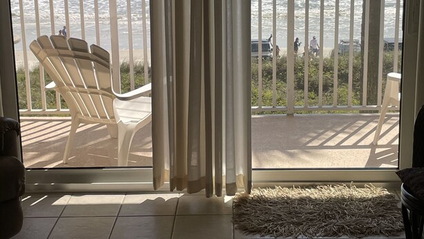 Une pièce avec vue sur l’océan, grâce à une grande fenêtre, un balcon avec des chaises et un tapis sur le sol.