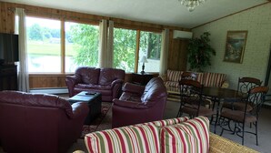 A living room with a large window, leather sofas, a wicker sofa, a dining table with chairs, and a painting on the wall. - Private Chalet with a View (Geneva)