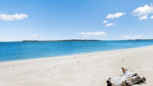 Une plage à l’eau d’un bleu cristallin, bordée d’un rivage sablonneux, avec une terre lointaine à l’horizon.