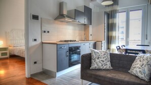 A modern apartment with a kitchenette, a sofa with patterned cushions, and a view through a window. - Three-room apartment in a strategic location between downtown and the sea CIN IT009002C2KQ9JCI5G (Albenga)