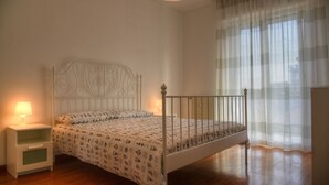 A bedroom with a white bed, a bedside table with a lamp, and sheer curtains on a window. - Three-room apartment in a strategic location between downtown and the sea CIN IT009002C2KQ9JCI5G (Albenga)