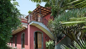 A building with a red facade, a balcony with a wooden railing, and a staircase leading to the entrance. - Holiday apartment with sea access on the Ionian Coast, Sicily (Torre Archirafi)