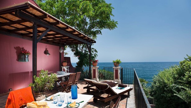 An outdoor dining area with a view of the sea, featuring a table set with plates, glasses, and cutlery, and a pergola overhead. - Holiday apartment with sea access on the Ionian Coast, Sicily (Torre Archirafi)