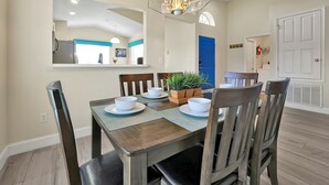 Un comedor con una mesa de madera, cuatro sillas y una araña.