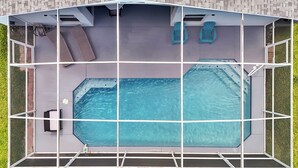 Una piscina en la azotea con cerramiento de vidrio, dos sillas azules y un jacuzzi.